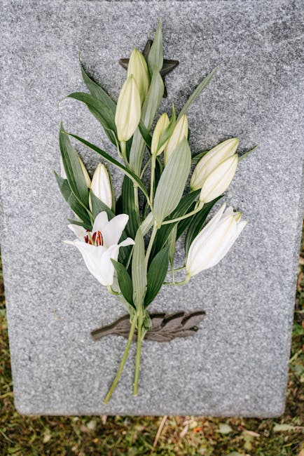 A delicate floral arrangement consisting of white lilies and white tulips placed against a grey stone surface. The lilies have large, open petals with prominent red stamens, while the tulips are in va