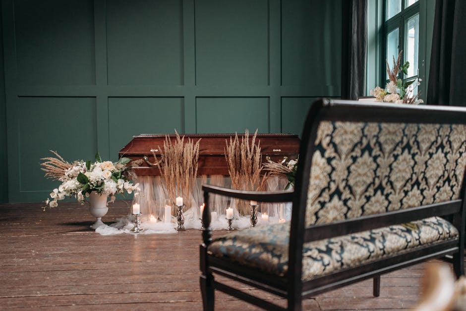 A floral arrangement resting on a wooden side table with a rich brown finish, featuring pampas grass and dried floral elements that add texture and neutral tones. To the left, a large white ceramic va