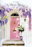 The photograph shows a peaceful, pastel-washed entrance that could easily belong to a new home on a calm street in Bow, moments after a thoughtful flower delivery. At the centre stands a pale pink door, painted in a soft, warm tone that radiates gentle welcome against the freshly whitewashed wall around it. The wall itself has a slightly textured surface, catching the light in faint, uneven patches that lend a sense of depth and quiet character. Overhead, a mature wisteria plant spills down in loose, abundant trails, its blossoms a mix of lavender and soft purple tones. The flower clusters hang like delicate tassels, forming a natural frame around the doorway and evoking a light, sweet fragrance you can almost sense. Nestled at the doorstep is a grey metal bucket, its simple, utilitarian shape softened by the lush bouquet it carries. Inside, creamy white roses with velvety petals open generously, mixed with subtle green foliage that adds contrast and a hint of movement. A satin ribbon in a gentle pink hue is wrapped around the bucket's base and tied in a modest bow, visually linking the arrangement to the colour of the door. The mild daylight creates soft, painterly shadows on the steps and wall, adding to the scene's calm, hopeful atmosphere. Altogether, the image feels like a quiet celebration of new beginnings in Bow, perfectly suited to a housewarming gift that turns a simple threshold into a place of comfort, optimism, and welcome.